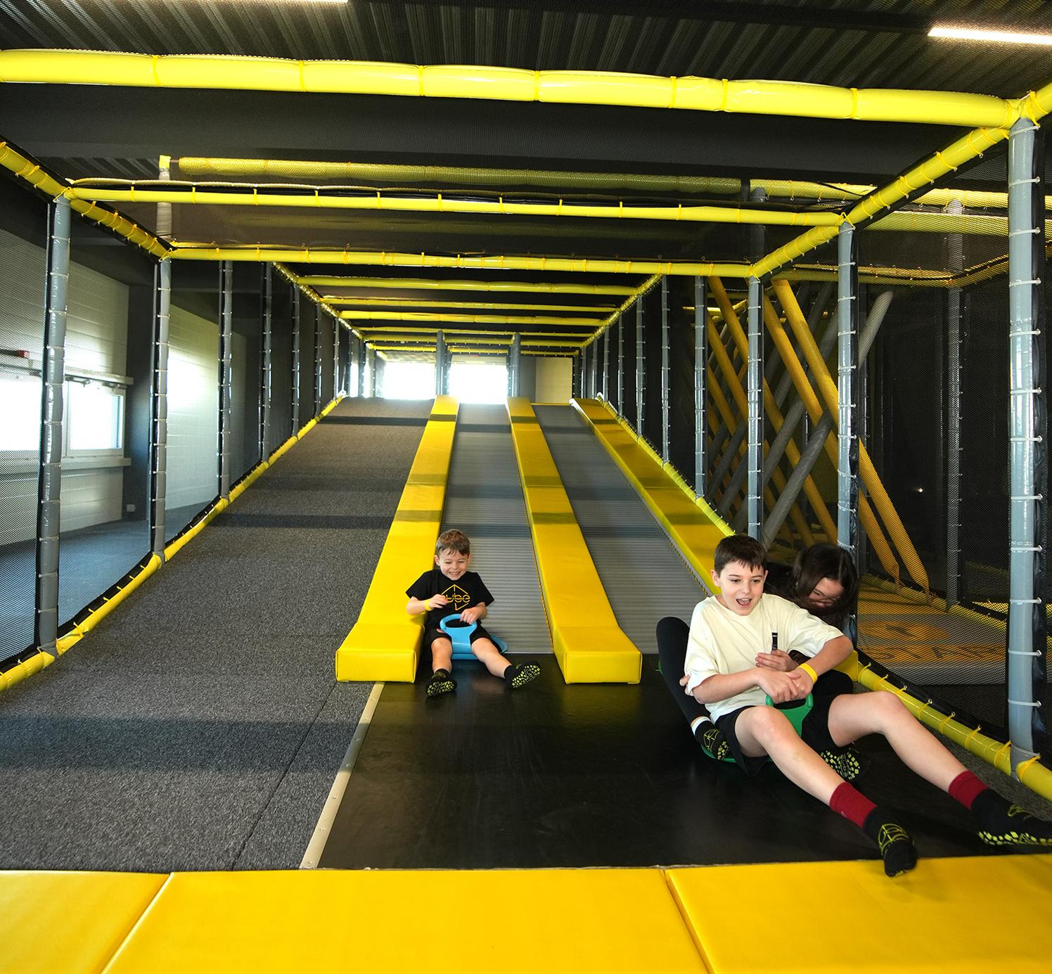 Kinder rutschen gemeinsam auf den Rollenrutschbahnen im CUBE